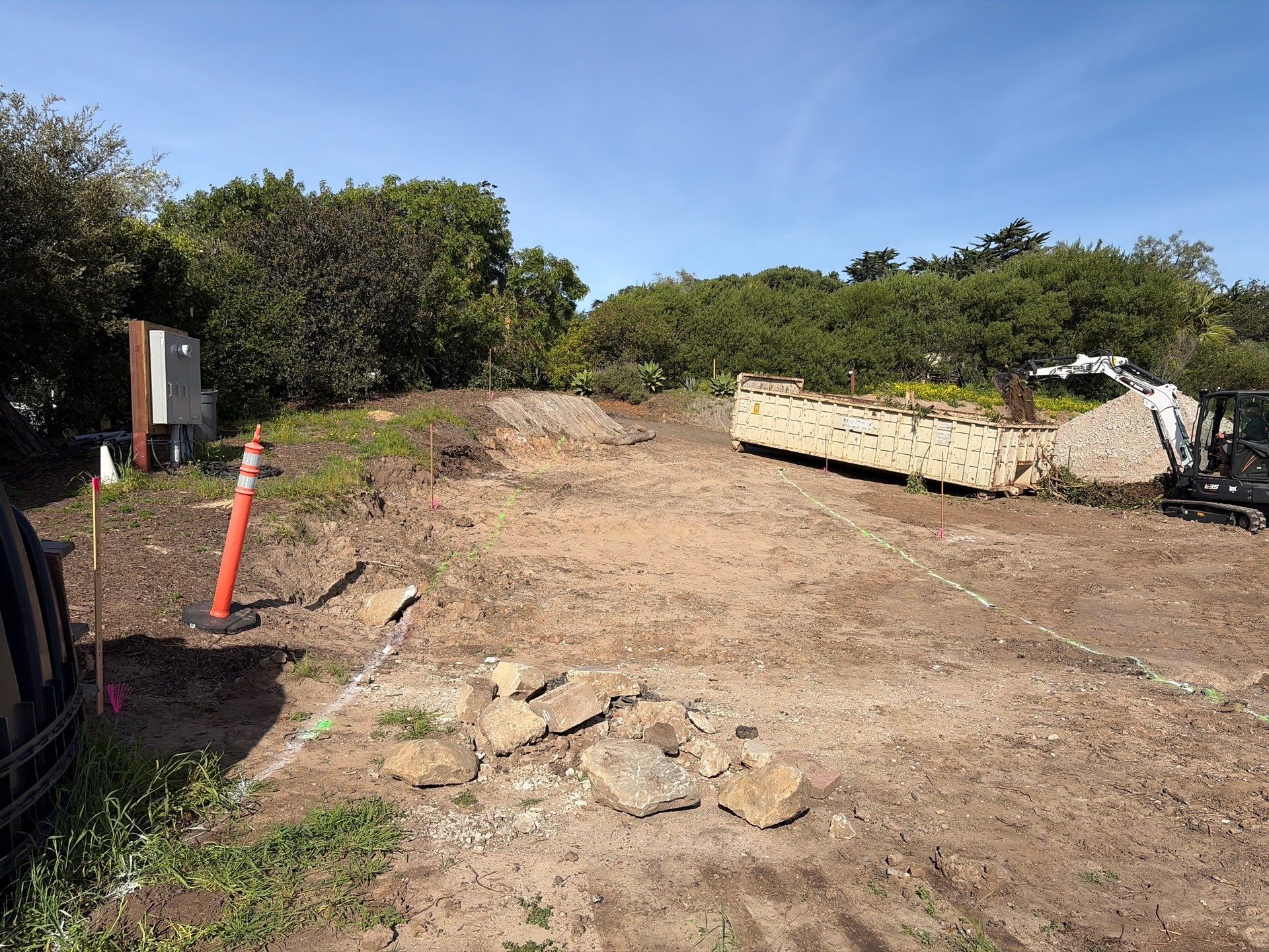 Driveway layout established with survey stakes marking the 3-foot overexcavation from edge of pavement
