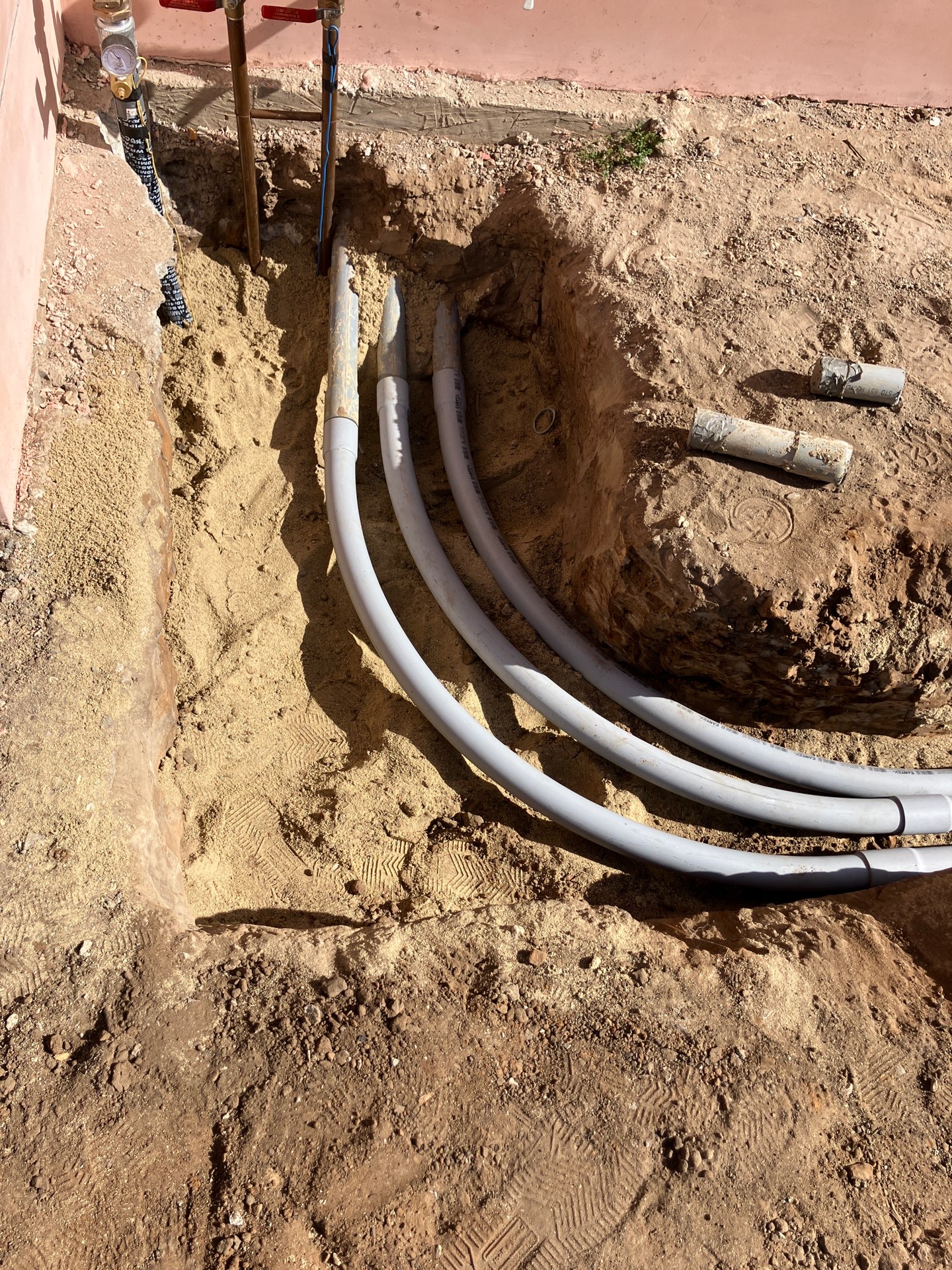 Conduit sweeps bending up out of the trench at a wall, the gentle radius that keeps wire pullable