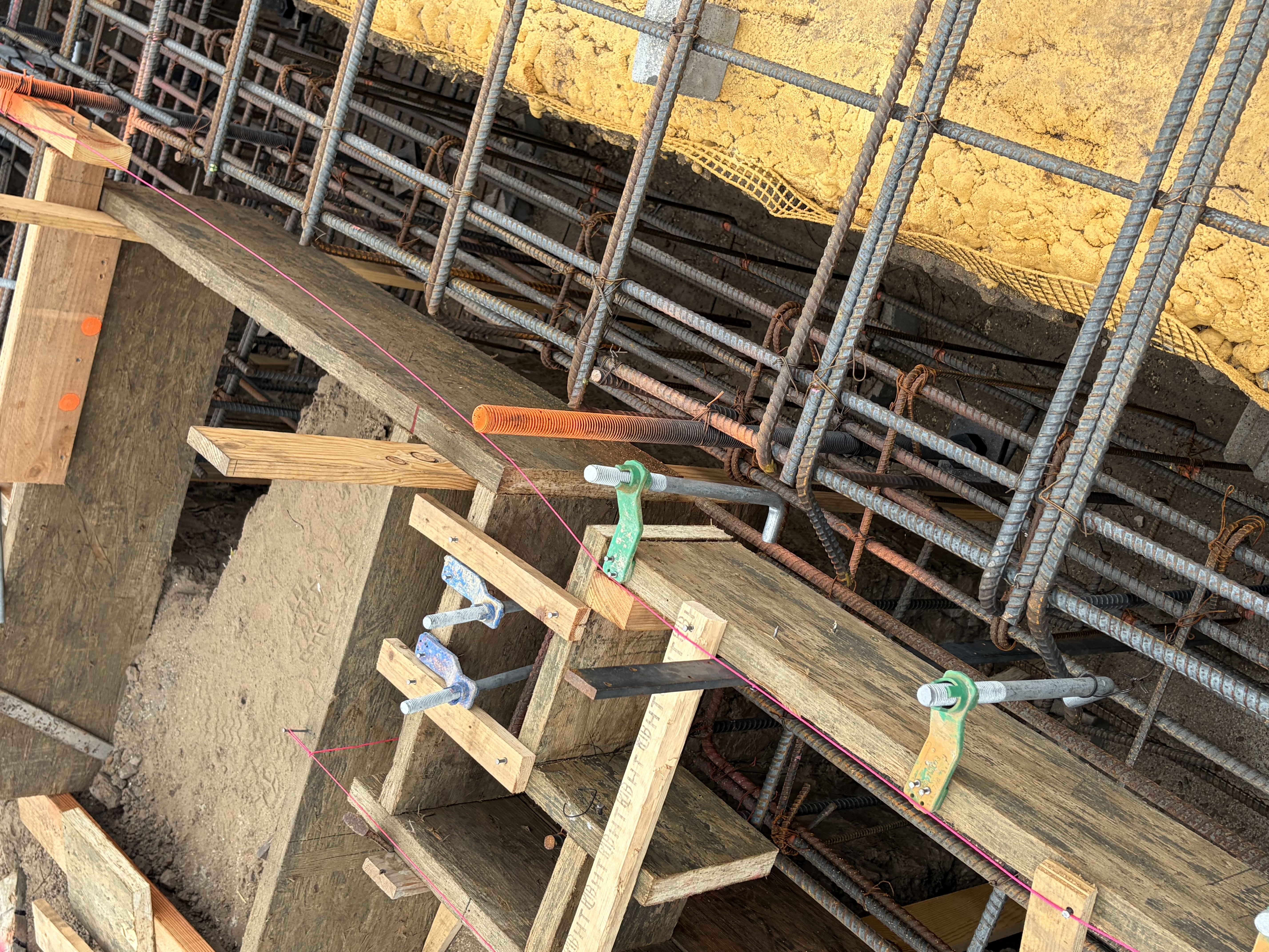 Anchor bolts set in the forms along a sill line before the pour, tagged and evenly spaced down the run