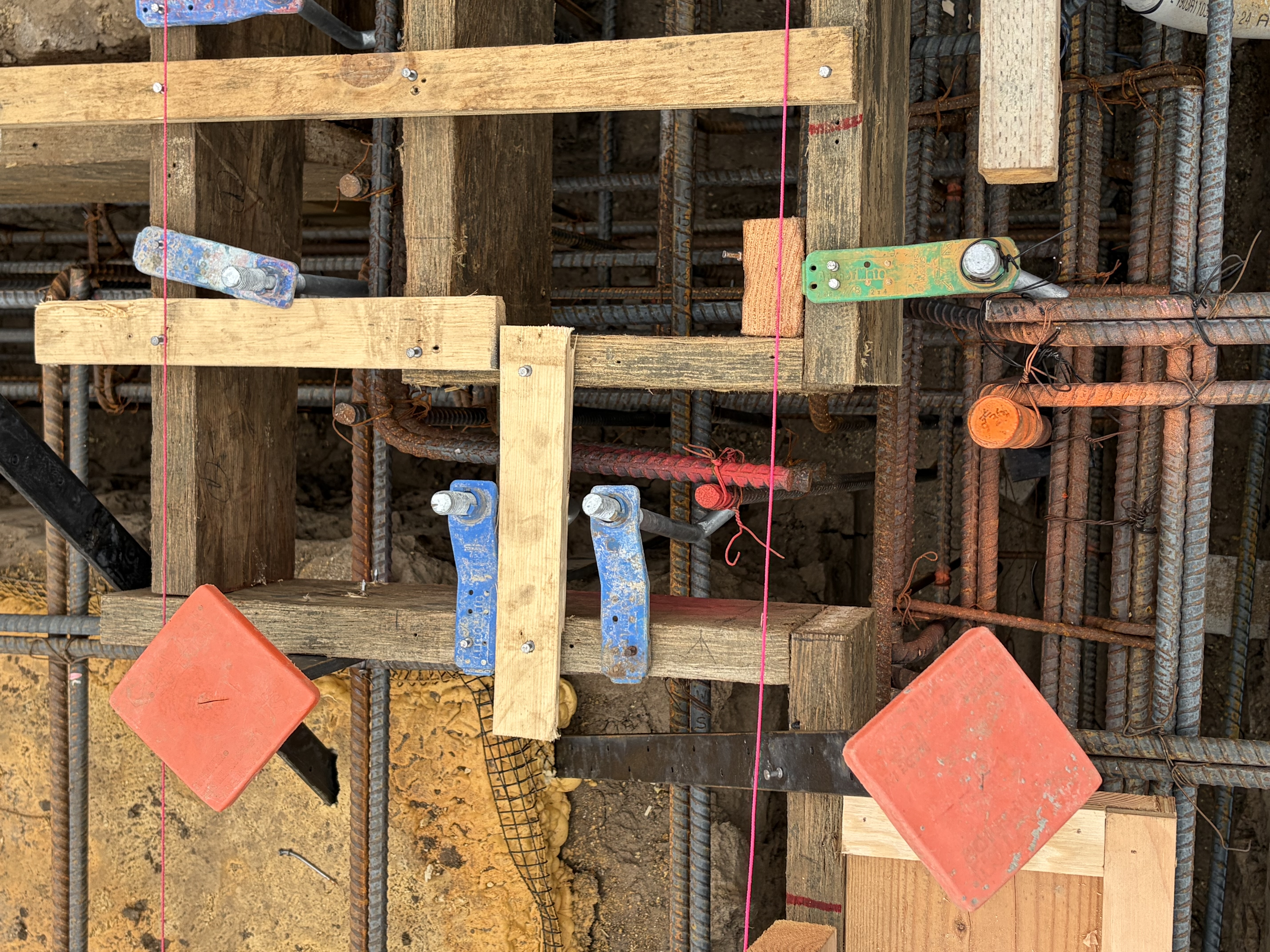 A row of Simpson hold-downs strapped to framing posts, their anchors cast into the rebar cage