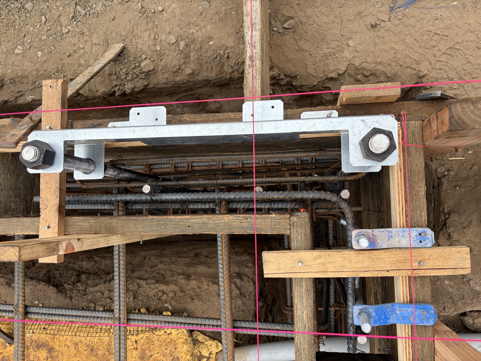 The galvanized template clamped to the cage, holding the anchor bolts and heavy hex nuts in position