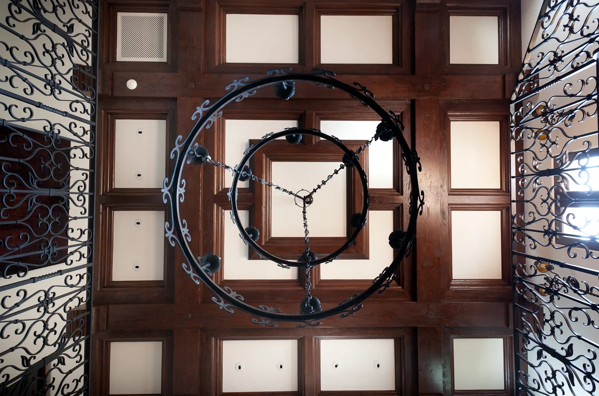 Wrought iron chandelier with coffered wood ceiling and ornate railing